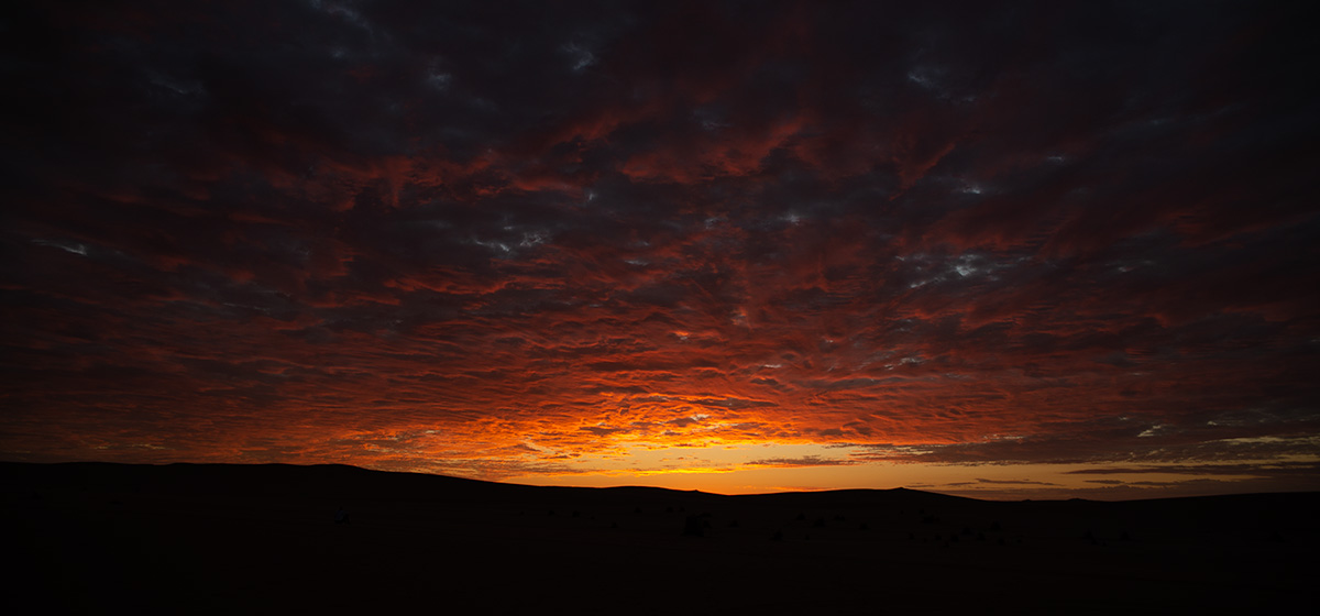 sunset - orange sun rays on the clouds with distant mountains silhouetted