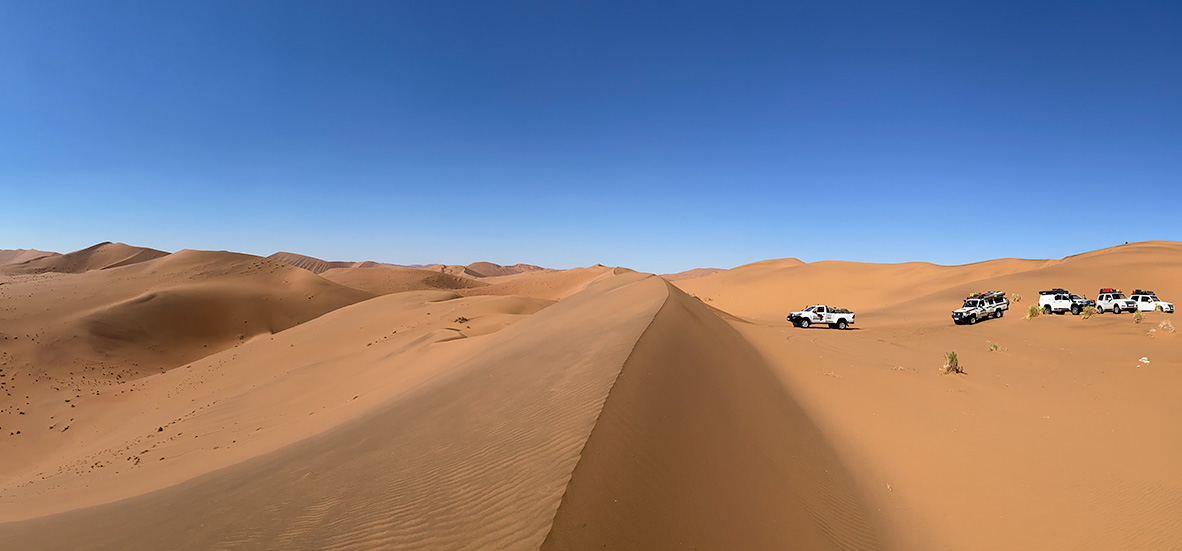 view from the crest of a dune with the vehicles in the distance
